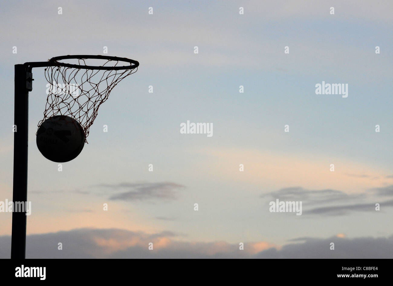 A Silhouette of a Netball going through a hoop with no players at dusk. Stock Photo