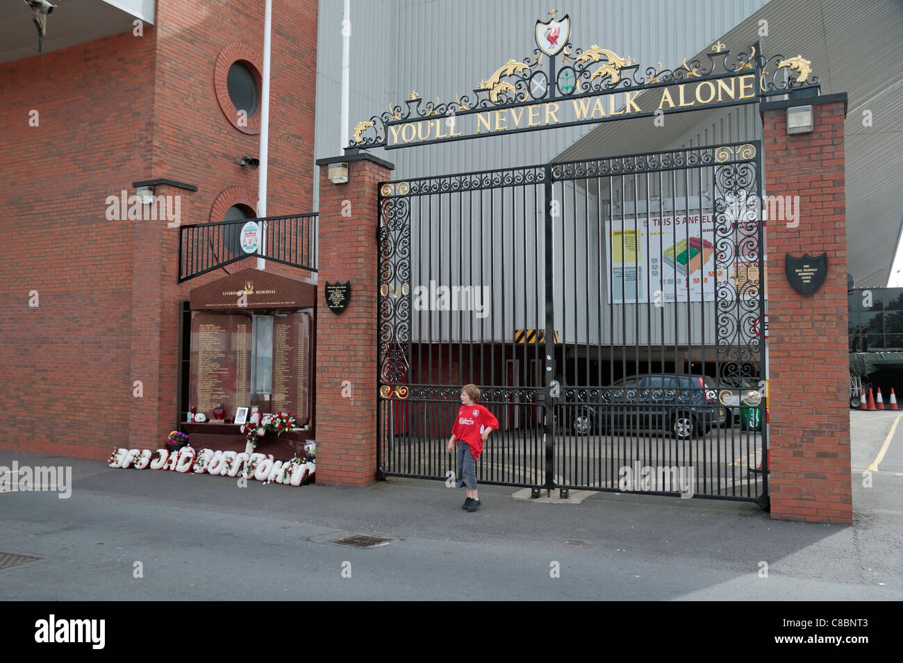 A young fan poses at the Anfield Road gates to Anfield, beside the Hillsborough disaster memorial, Liverpool football club. Stock Photo