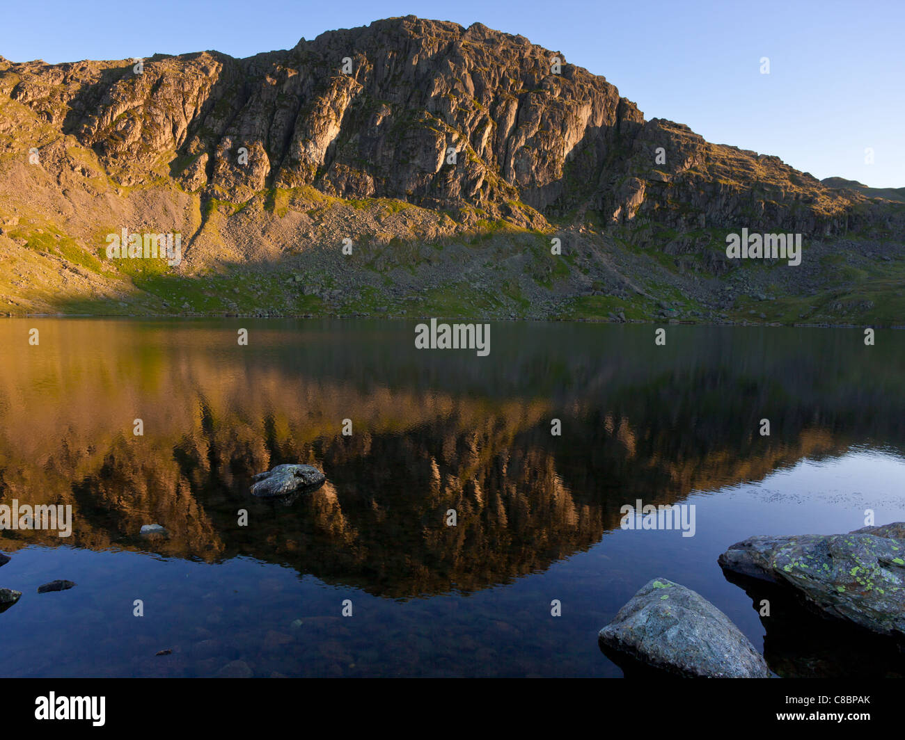 The cliffs of Pavey Ark across Stickle Tarn shortly after sunrise.  English Lake District. Stock Photo