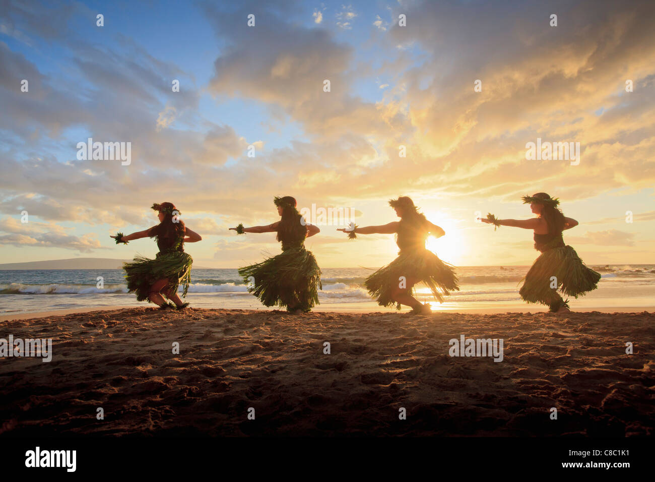 Four hula dancers at sunset at Palauea, Maui, Hawaii, back lit by the sun. Stock Photo