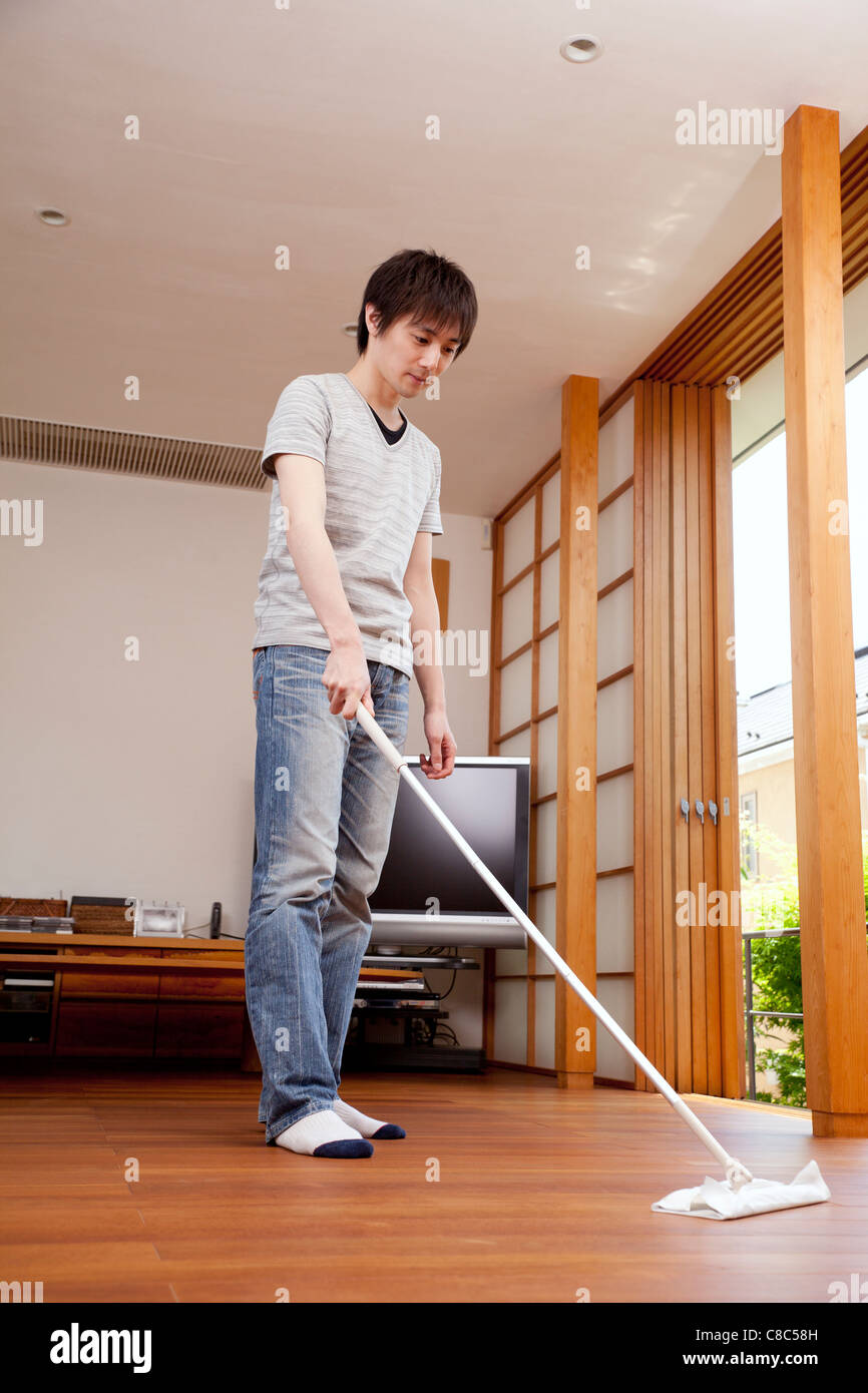 Young man sweeping floor with floor mop Stock Photo