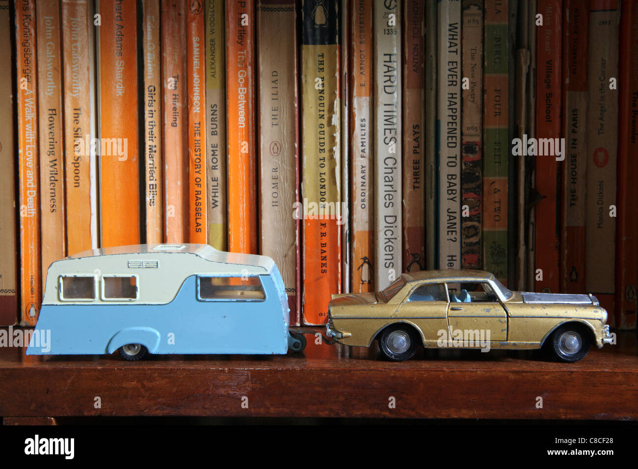 Vintage Dinky toy Rolls Royce, towing caravan, along front of bookshelf with paperback novels behind Stock Photo
