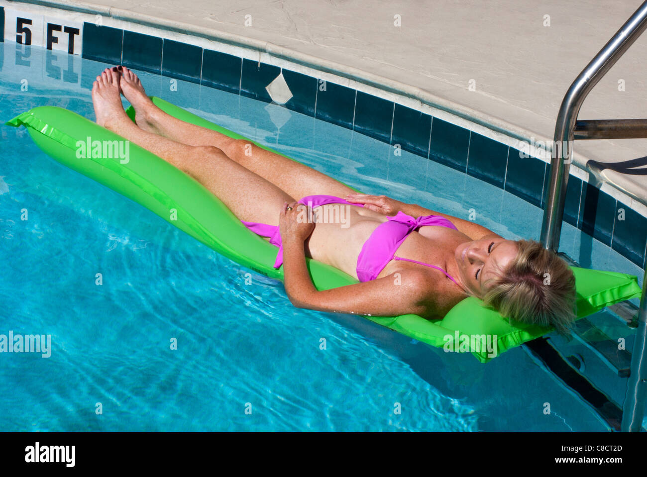 woman sunbathing on a lilo at the edge of a swimming pool. Stock Photo