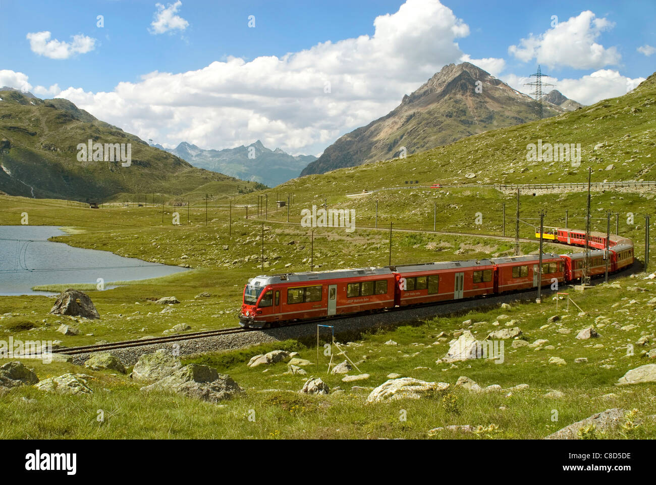 Alpine train in a mountain landscape at Lago Bianco, Bernina Pass, Grisons, Switzerland in summer Stock Photo