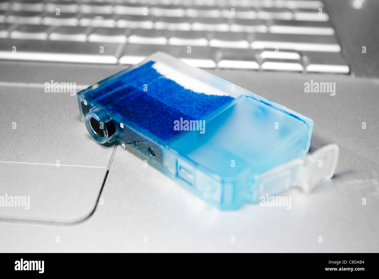 Almost empty blue inkjet cartridge lying on laptop. Stock Photo