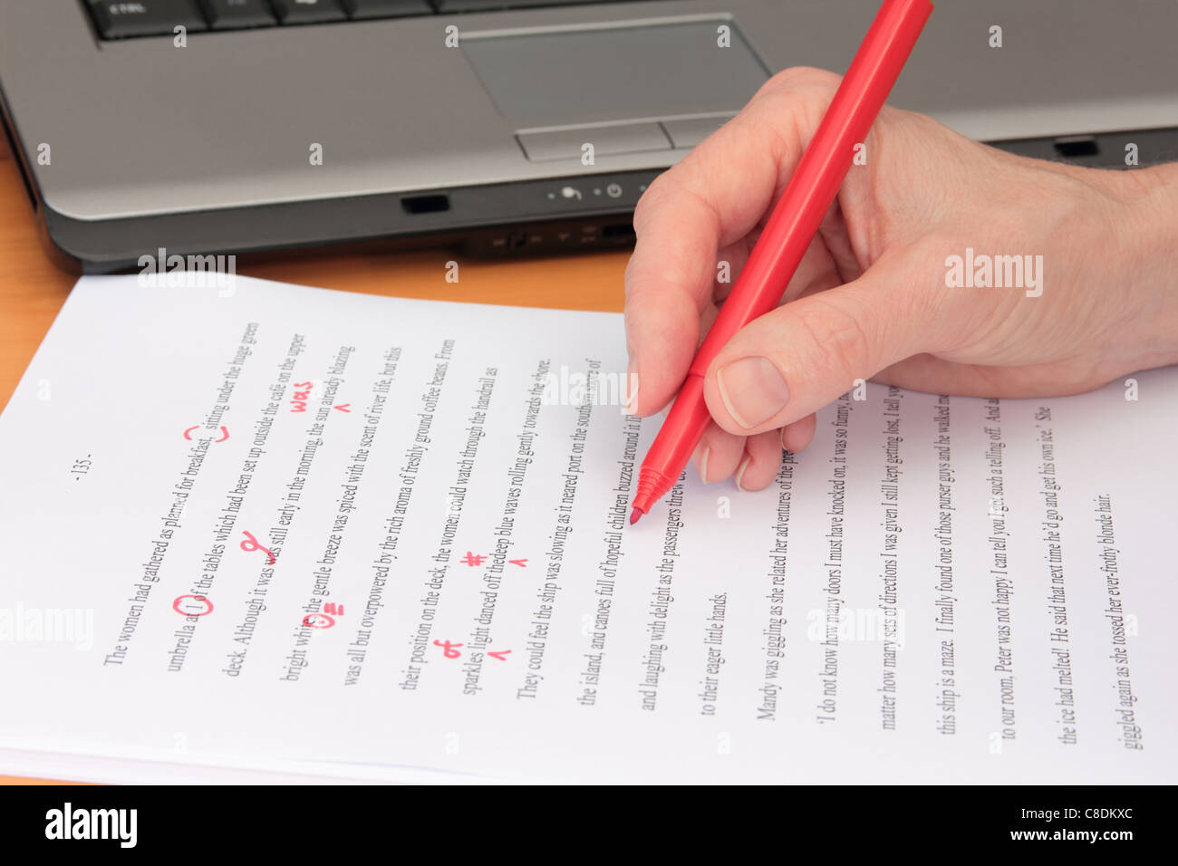 Hand Proofreading a Manuscript beside Laptop Stock Photo
