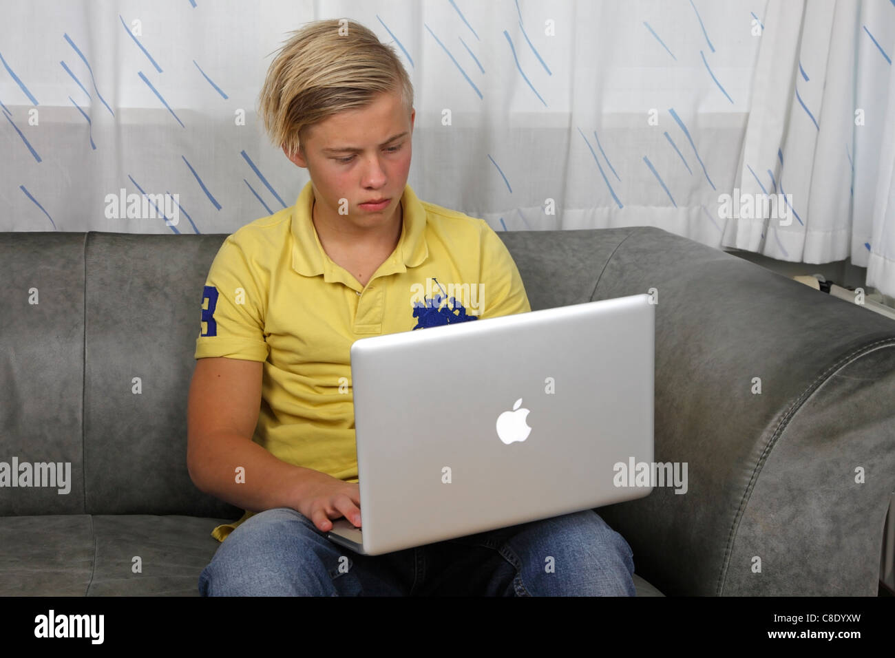 Teenager using his Apple MacBook Pro for homework while keeping his friends up-to-date on the social networks Stock Photo