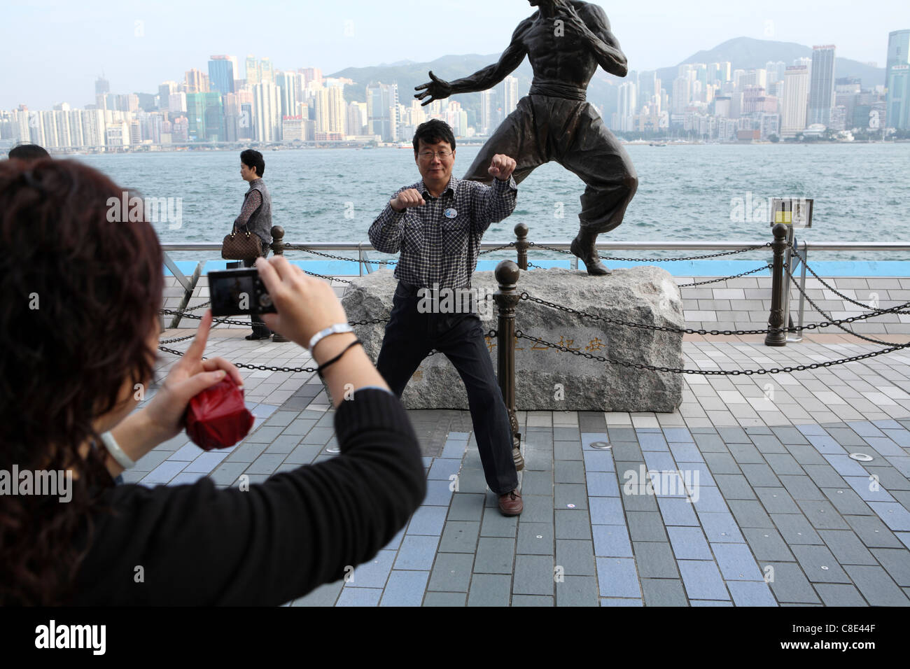 A tourist poses for photography by statue of Hong Kong martial arts and film star Bruce Lee (1940-73) on the Avenue of the Stars Stock Photo