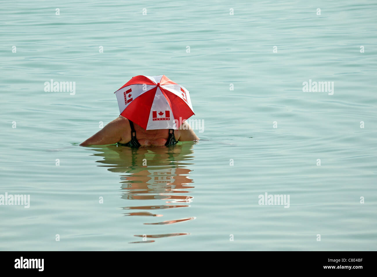 Lady in Red and White Umbrella Hat marked with Canadian Flag in The Dead Sea, Israel. Stock Photo