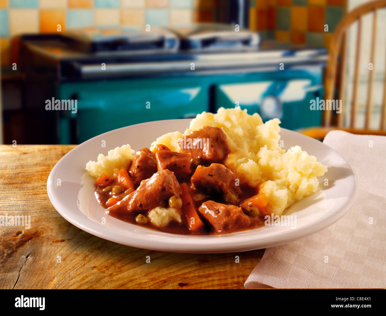 Traditional braised lamb casserole & mashed potato served on a plate on a wood table in a kitchen setting Stock Photo