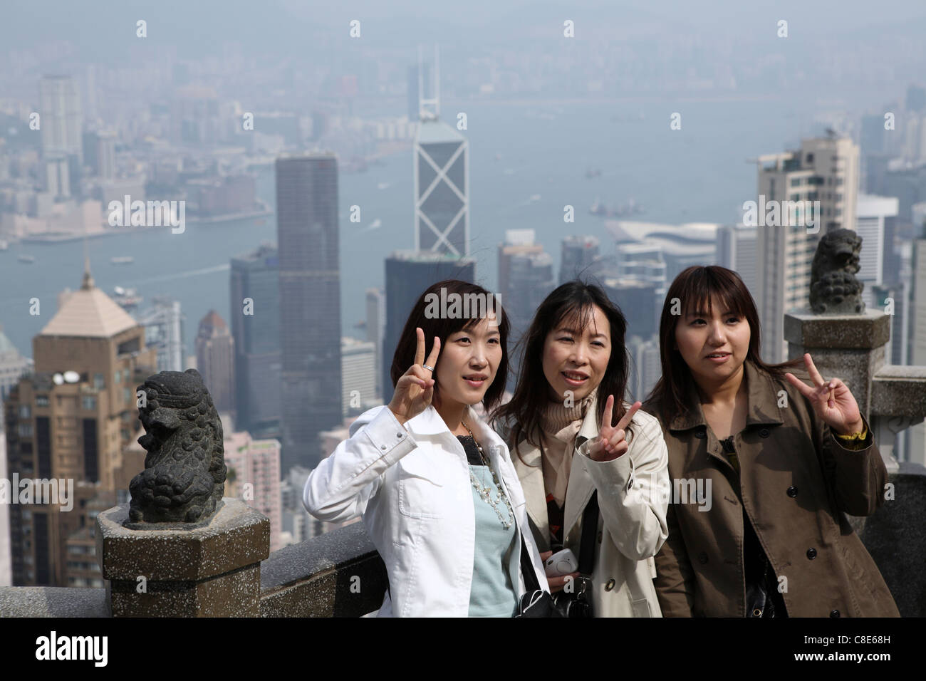 three young Asian Chinese women pose for a photograph The Peak, view overlooking Victoria Harbor & Skyscrapers, Hong Kong, China Stock Photo