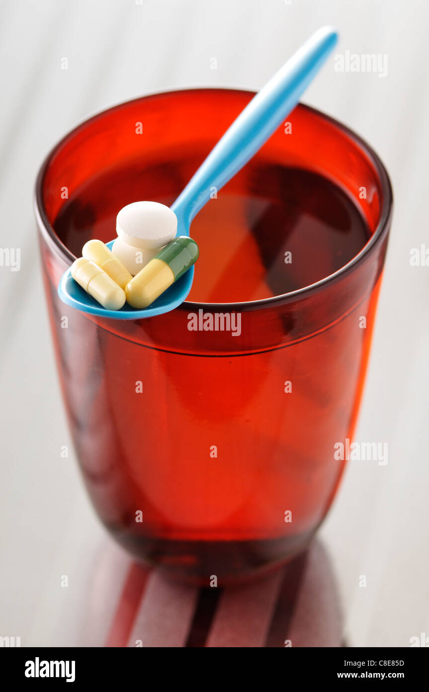 Spoonful of pills and glass of water Stock Photo