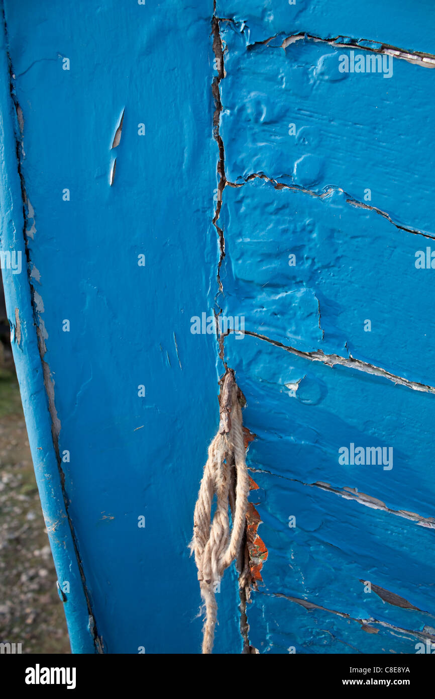 Blue paint flaking off an old boat, cracking the wood open at the bow