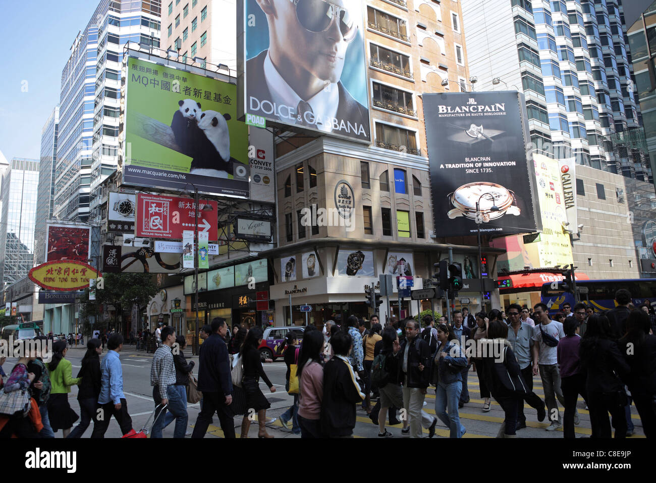 busy shopping street Kowloon, Hong Kong, China, dozens cross at traffic lights under billboards for high end branded goods Stock Photo