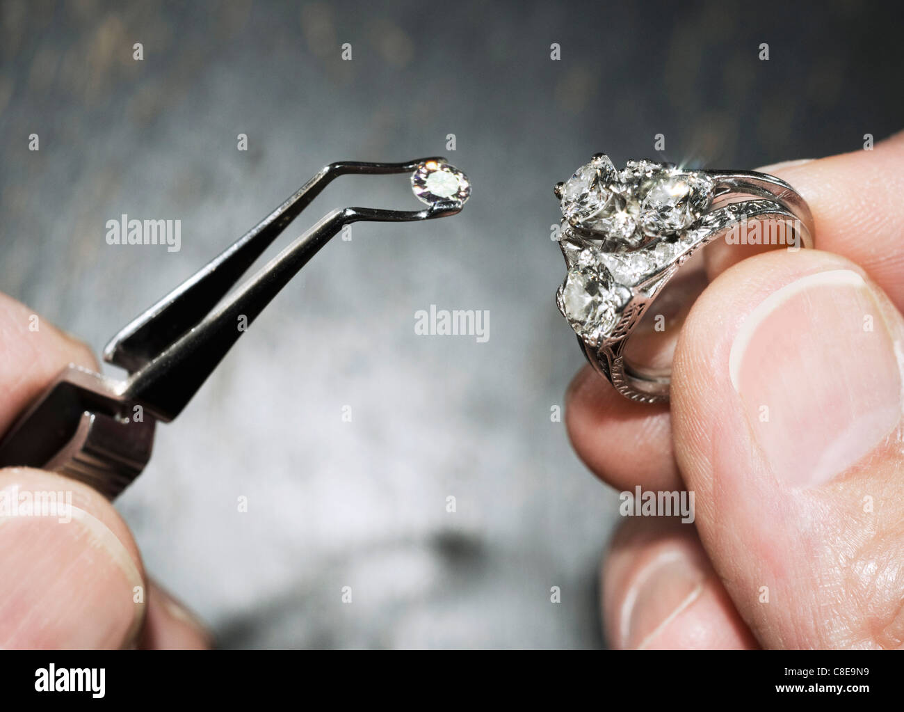 hands holding diamond ring with gem in tweezers Stock Photo