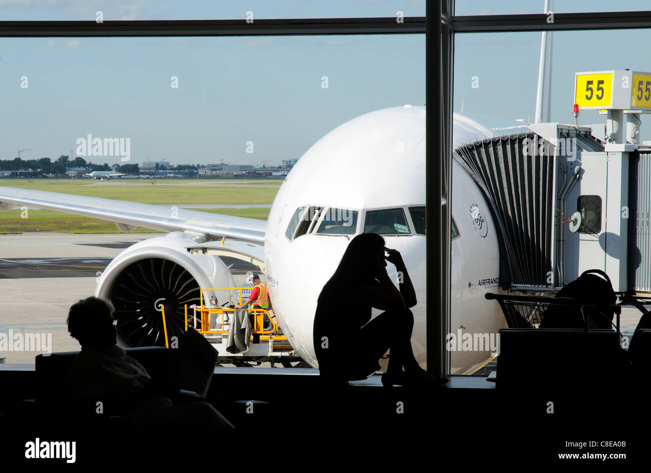 A young woman on a mobile phone in silhouette in an airport departure lounge window with a plane behind Stock Photo