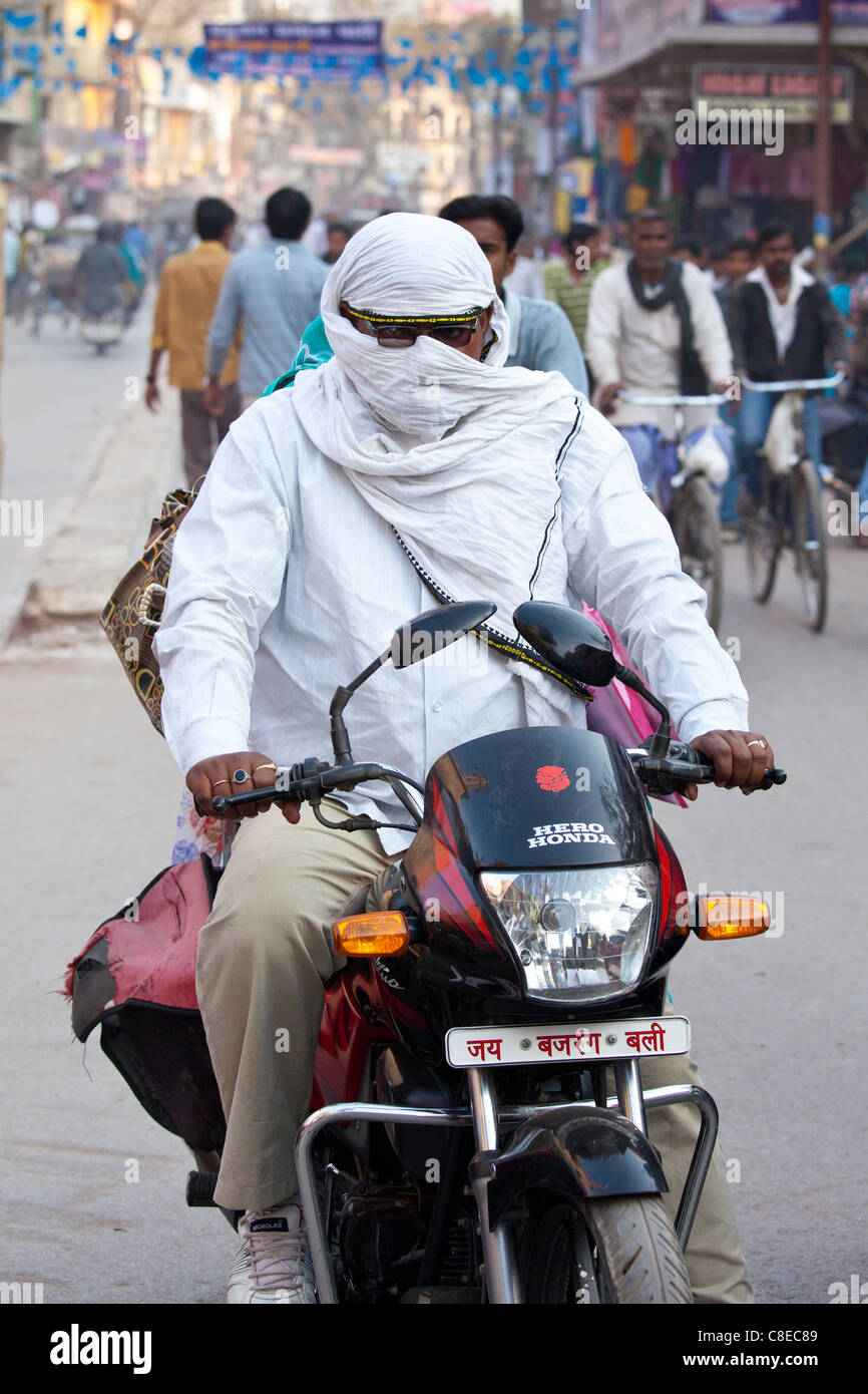Man driving Hero Honda motorcycle with covered head and face in street scene in city of Varanasi, Benares, Northern India Stock Photo