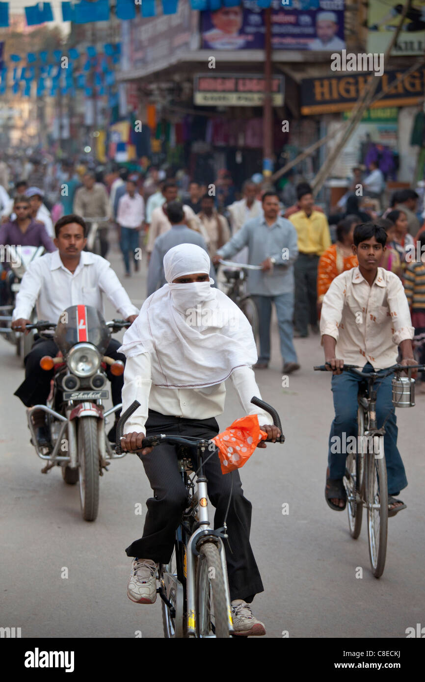 Muslim woman with hijab burkha veil covering head and face cycles in the street in city of Varanasi, Benares, Northern India Stock Photo