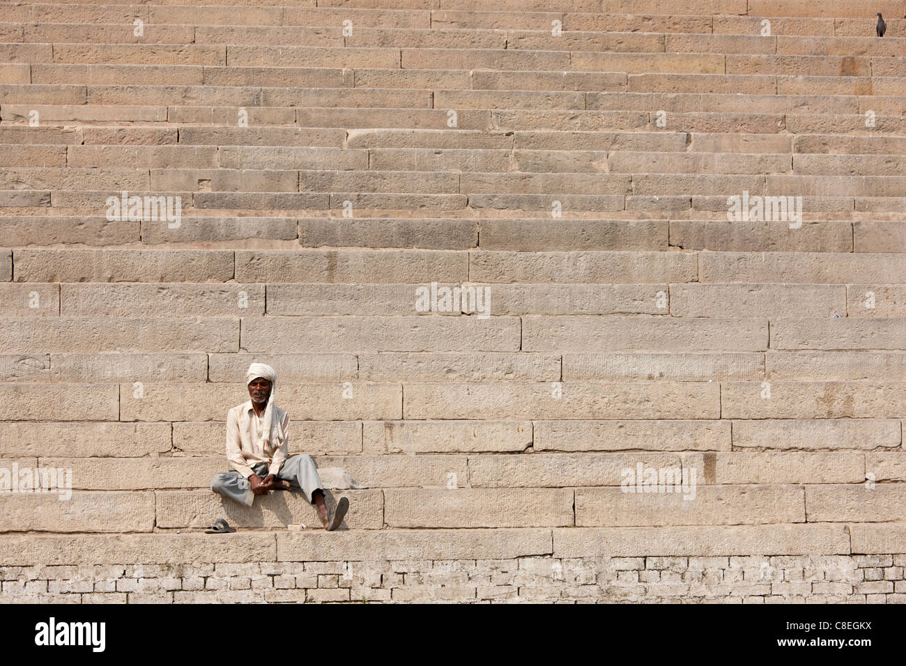 Hindu man sits on steps of Chet Singh Ghat on banks of The Ganges River in holy city of Varanasi, India Stock Photo