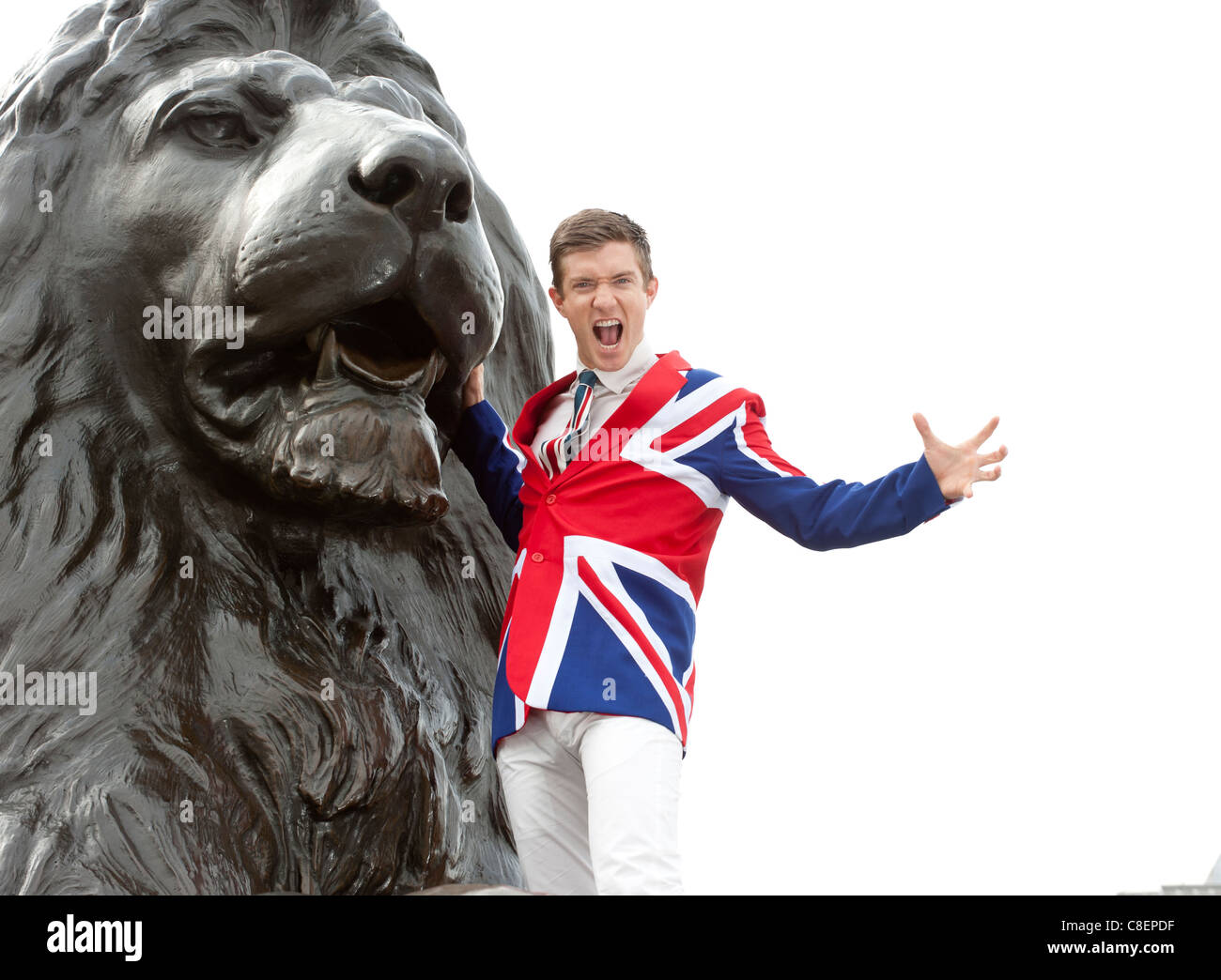 Young man wearing Union Flag jacket roaring next to the lion statue,  Trafalgar Square, London, England Stock Photo