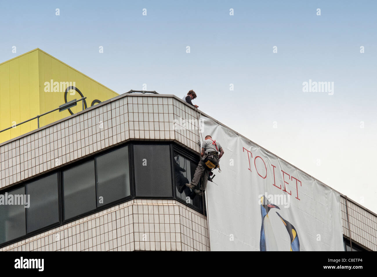men working on top of a building hanging an advertising banner Stock Photo
