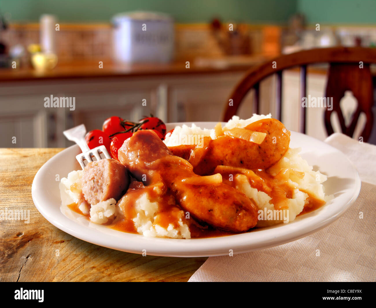 Traditional cooked Sausage and mash served on a white plate in a table setting ready to eat Stock Photo