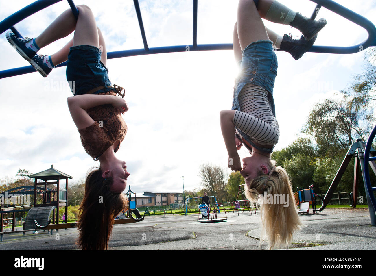 Two 16 17 year old teenage girls, hanging upside down in a playground, UK Stock Photo