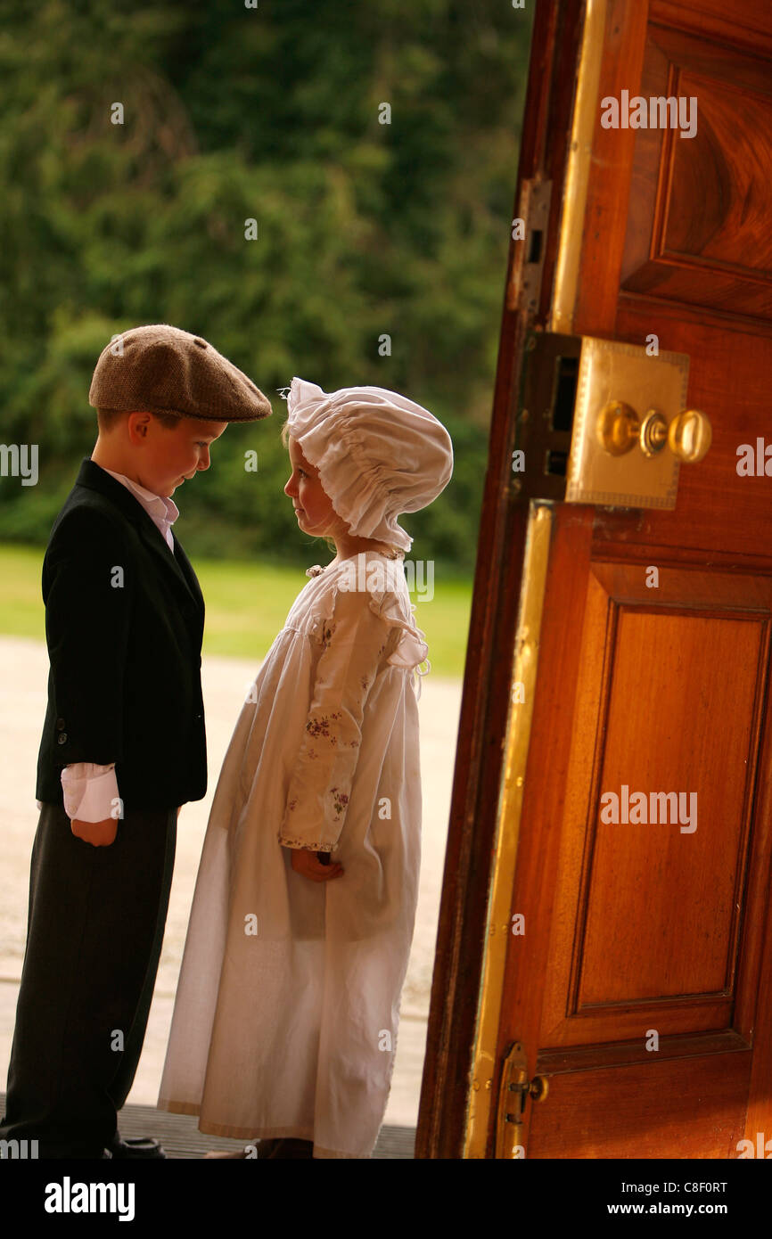 Two young children in Victorian costume stand near a 18th century