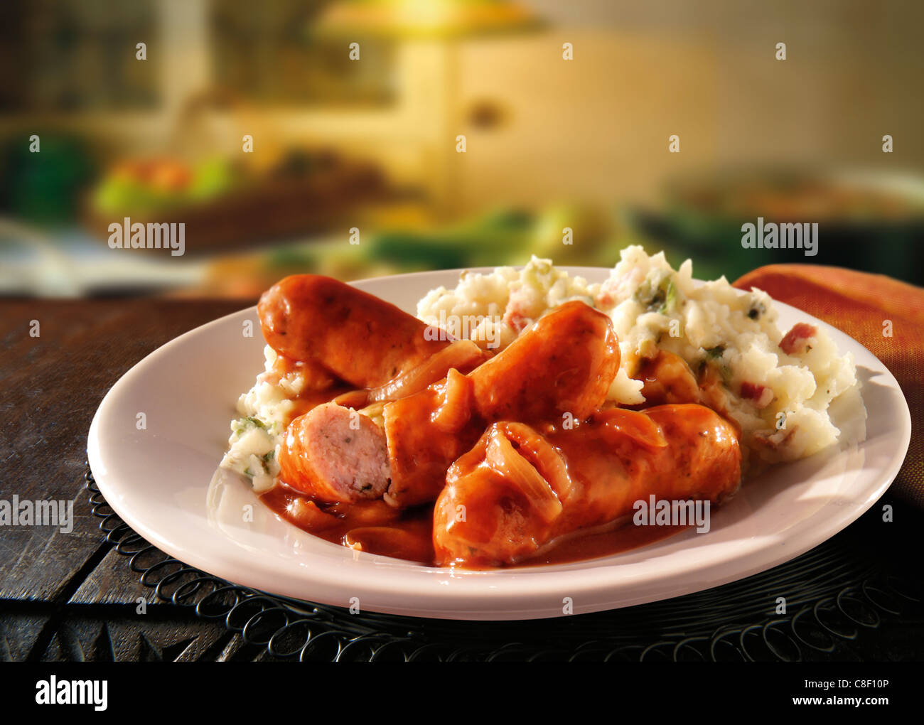 Traditional cooked Sausage and mash served on a white plate in a table setting ready to eat Stock Photo