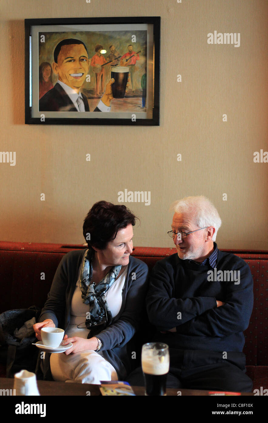 Two elderly people enjoy a pint and a cup of tea as a picture of US president Barack Obama hangs above them in a Irish pub Stock Photo