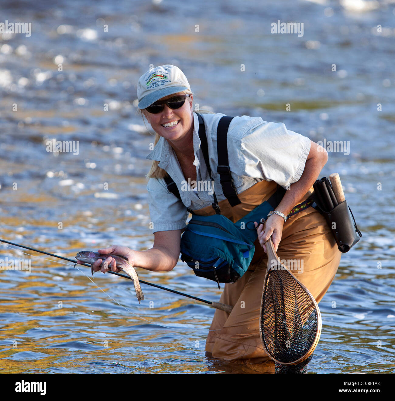 A woman female fly-fishing with a freshly caught rainbow trout in
