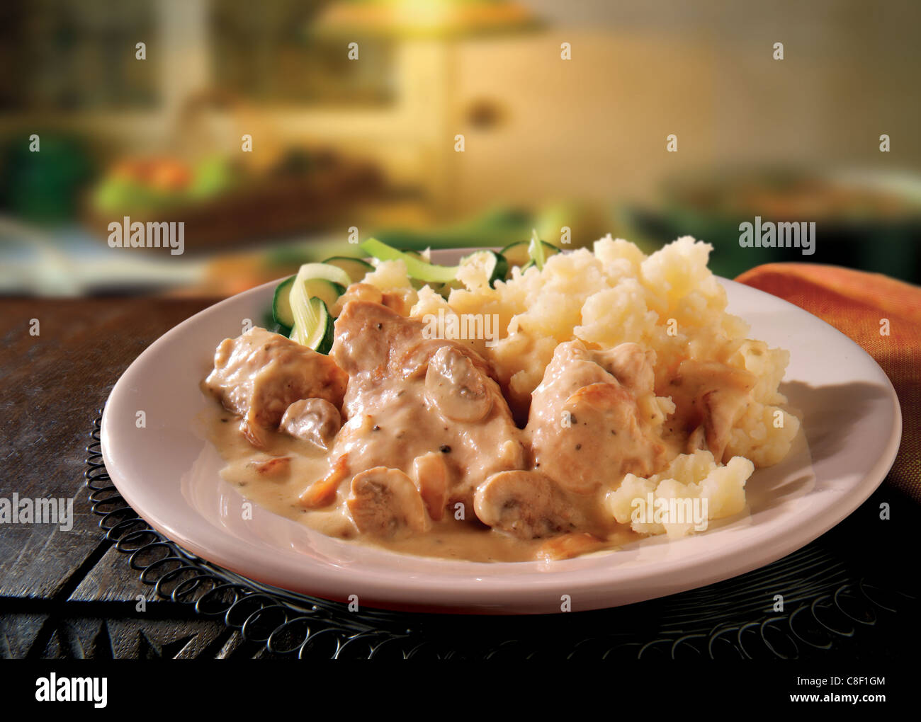 Traditional cooked British pork and apple casserole served on a white plate on a table in a traditional kitchen setting Stock Photo