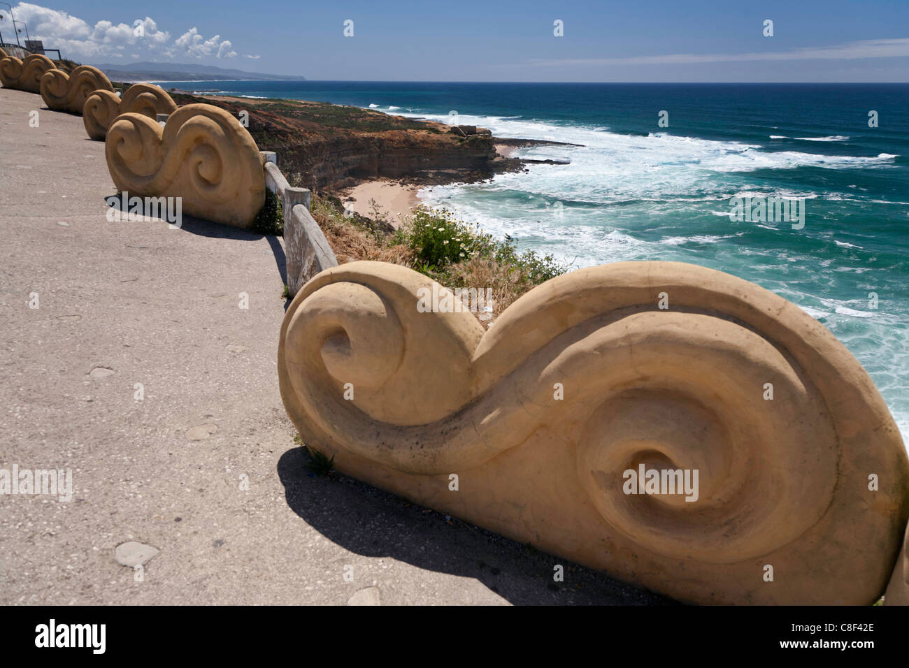 Ericeira, Portugal, cliff top with decorative wave-shaped wall looking south at the blue rolling surf Stock Photo