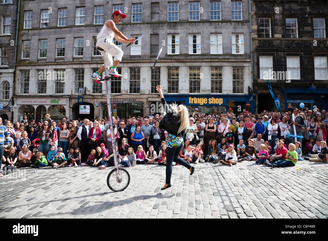 Juggler at Edinburgh Festival on a unicycle getting a woman to throw knives for him to catch Stock Photo