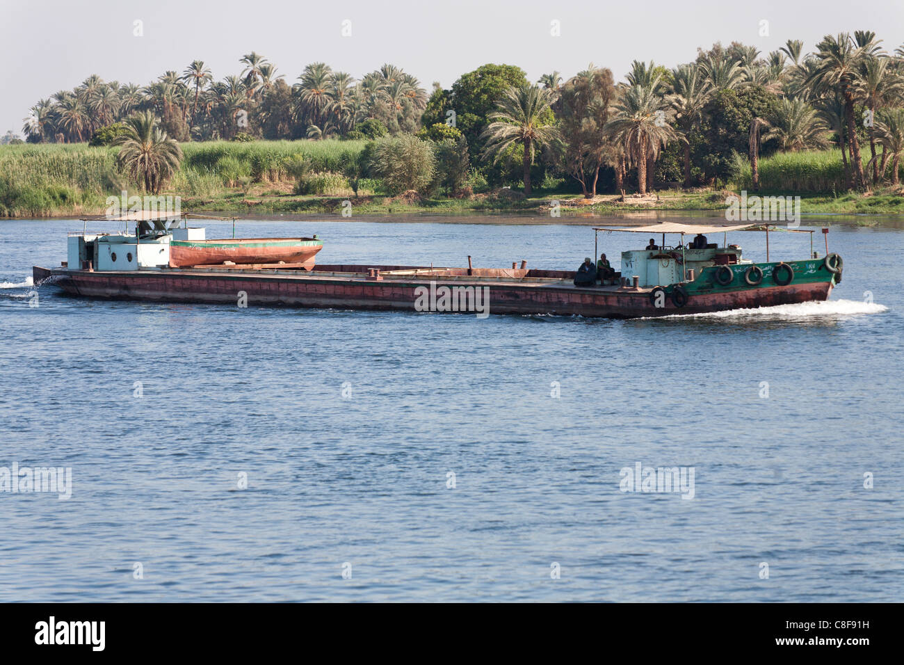 A  section of Nile river bank  with tug boat sailing left to right with palms and grassy bank in background, Egypt Stock Photo
