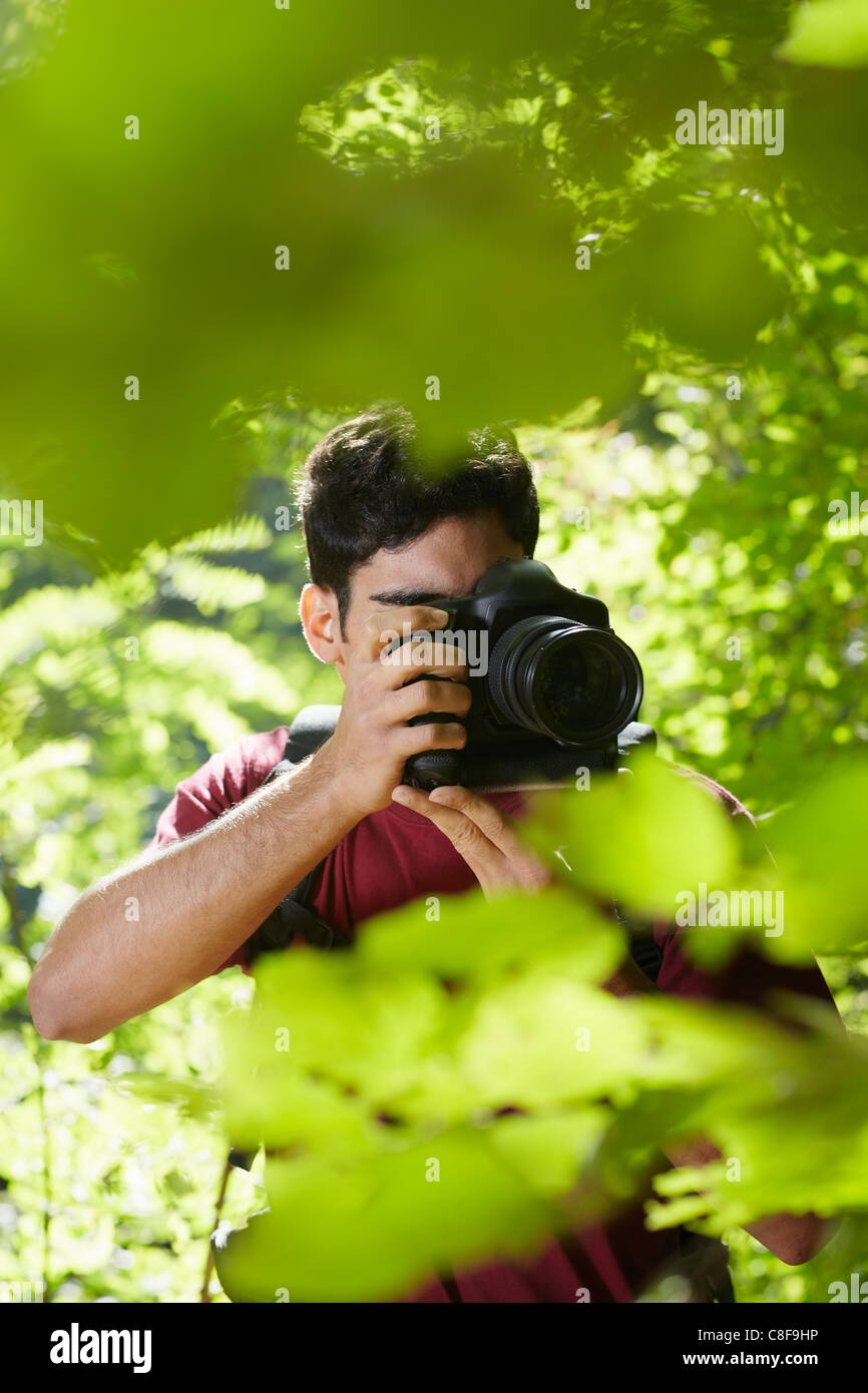 young hispanic man trekking among trees and taking pictures with dslr camera. Vertical shape, front view, copy space Stock Photo