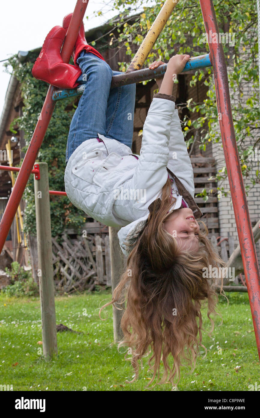 young girl hanging off monkey bars Stock Photo