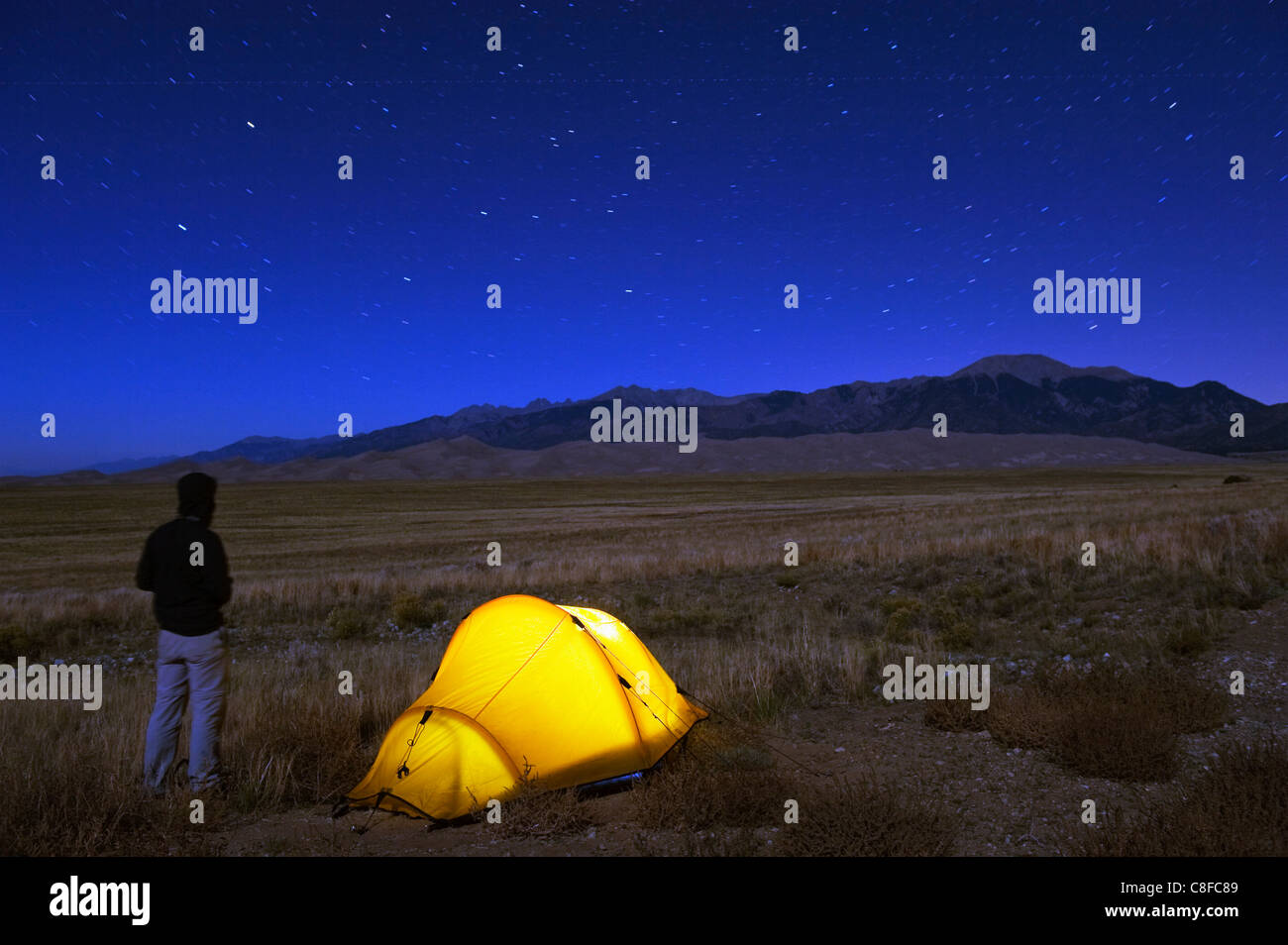Hiker and tent illuminated under the night sky, Great Sand Dunes National Park, Colorado, United States of America Stock Photo