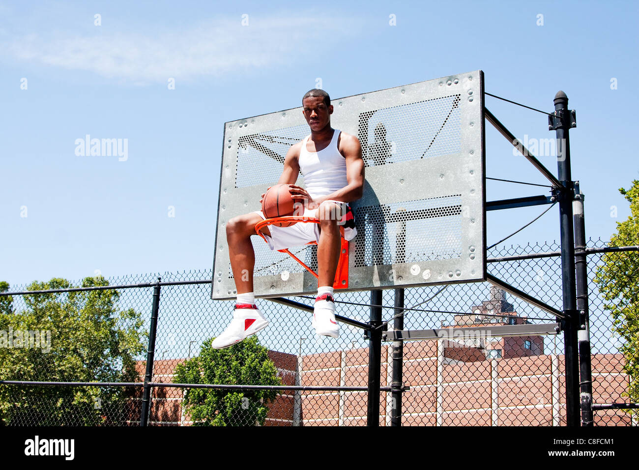 Basketball player sitting in hoop Stock Photo
