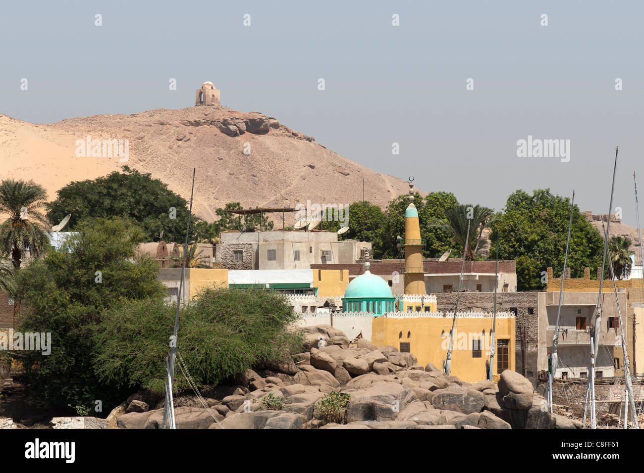 Village settlement seen from the Nile with houses and mosque and shrine on a hill in the background, Aswan, Egypt, Africa Stock Photo