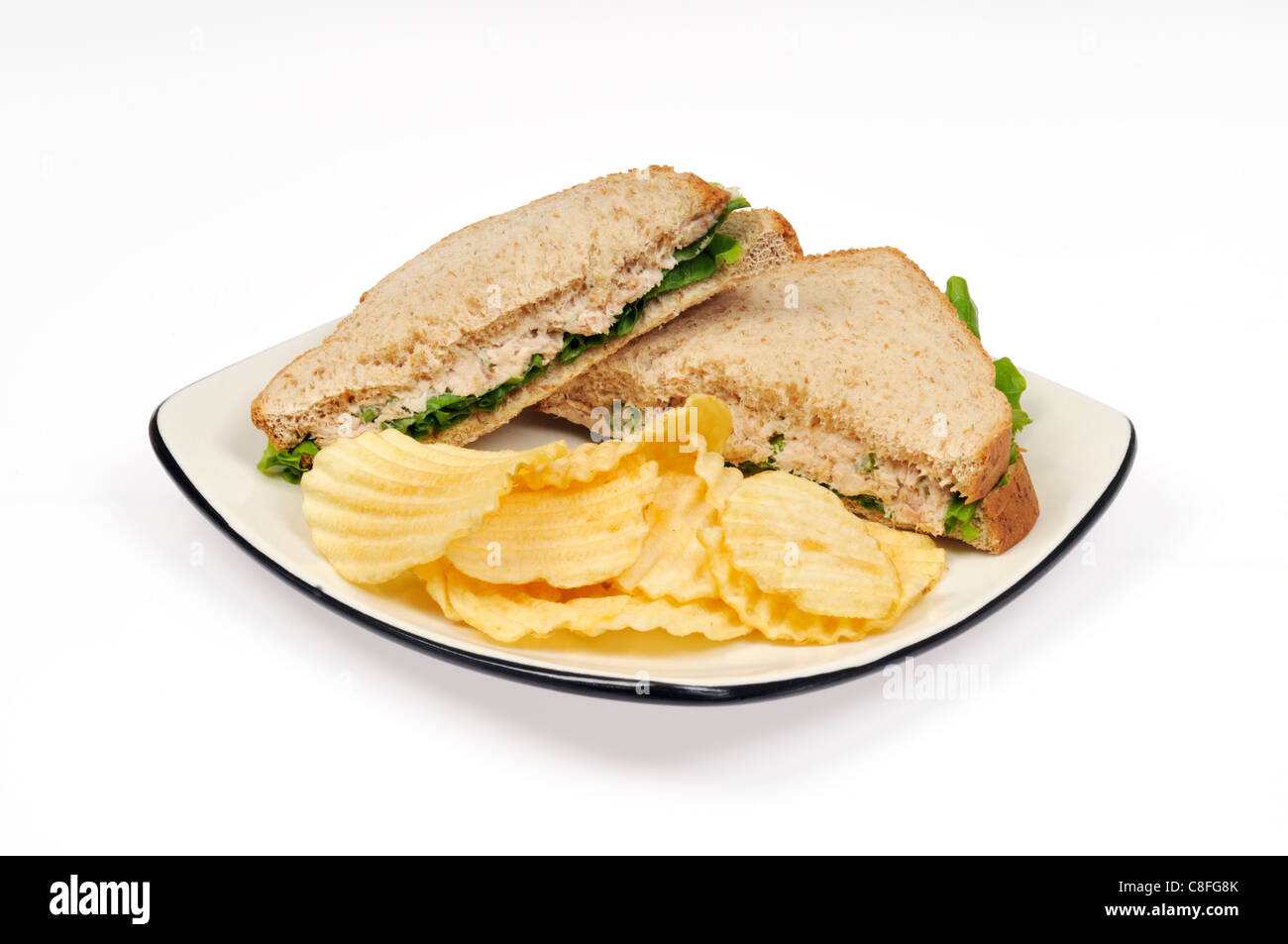 Tuna mayo with lettuce on wholemeal bread sandwich with potato chips on white plate on white background cutout. Stock Photo