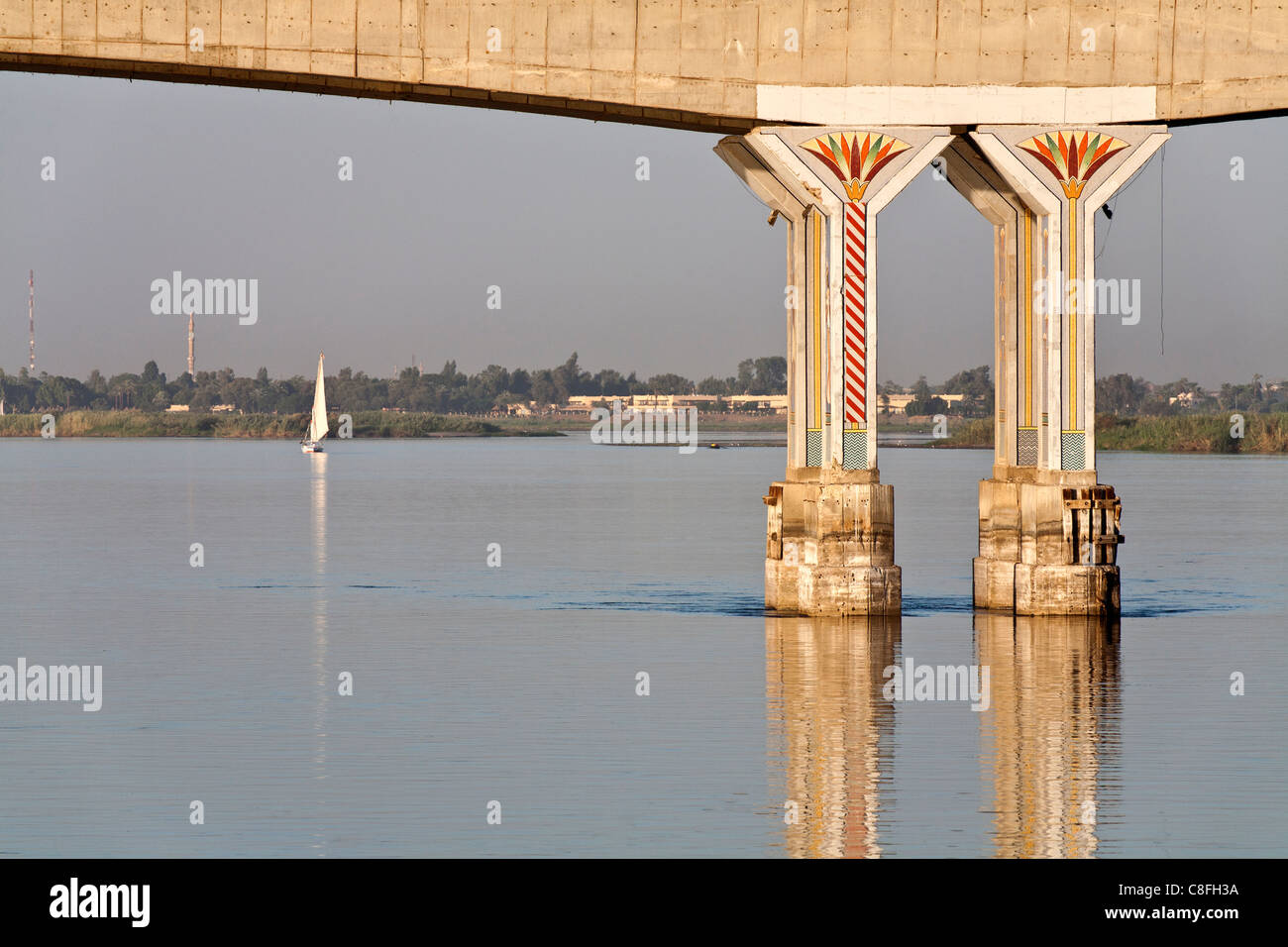 Two decorated pillars of Luxor bridge seen from the middle of the Nile reflected in calm water,with distant felucca, Egypt, Stock Photo