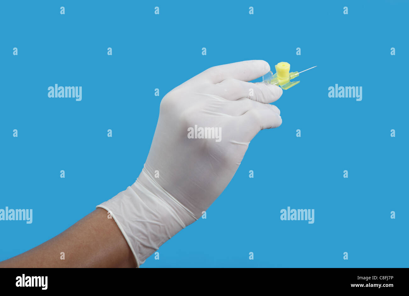 Hand in surgical glove holding a small intravenous needle against a blue background. Stock Photo