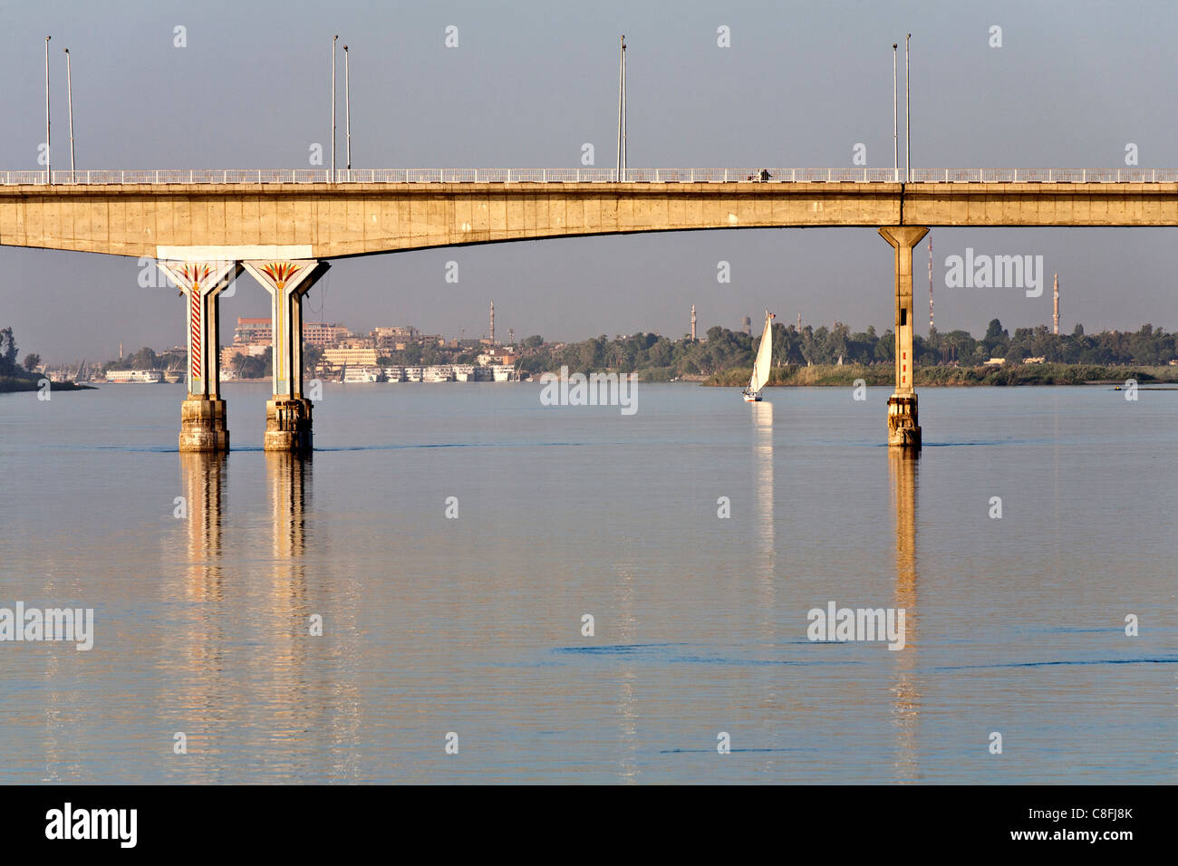 Section of Luxor bridge seen from the middle of the Nile reflected in calm water, with felucca in distance Luxor, Egypt, Africa Stock Photo