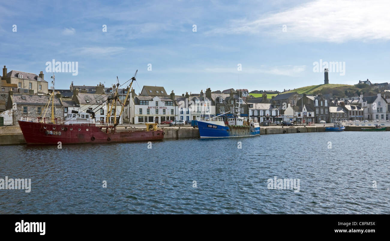 Trawlers tied up along the harbour quay in Macduff Aberdeenshire with The Macduff war memorial octagonal Tower behind on hill. Stock Photo