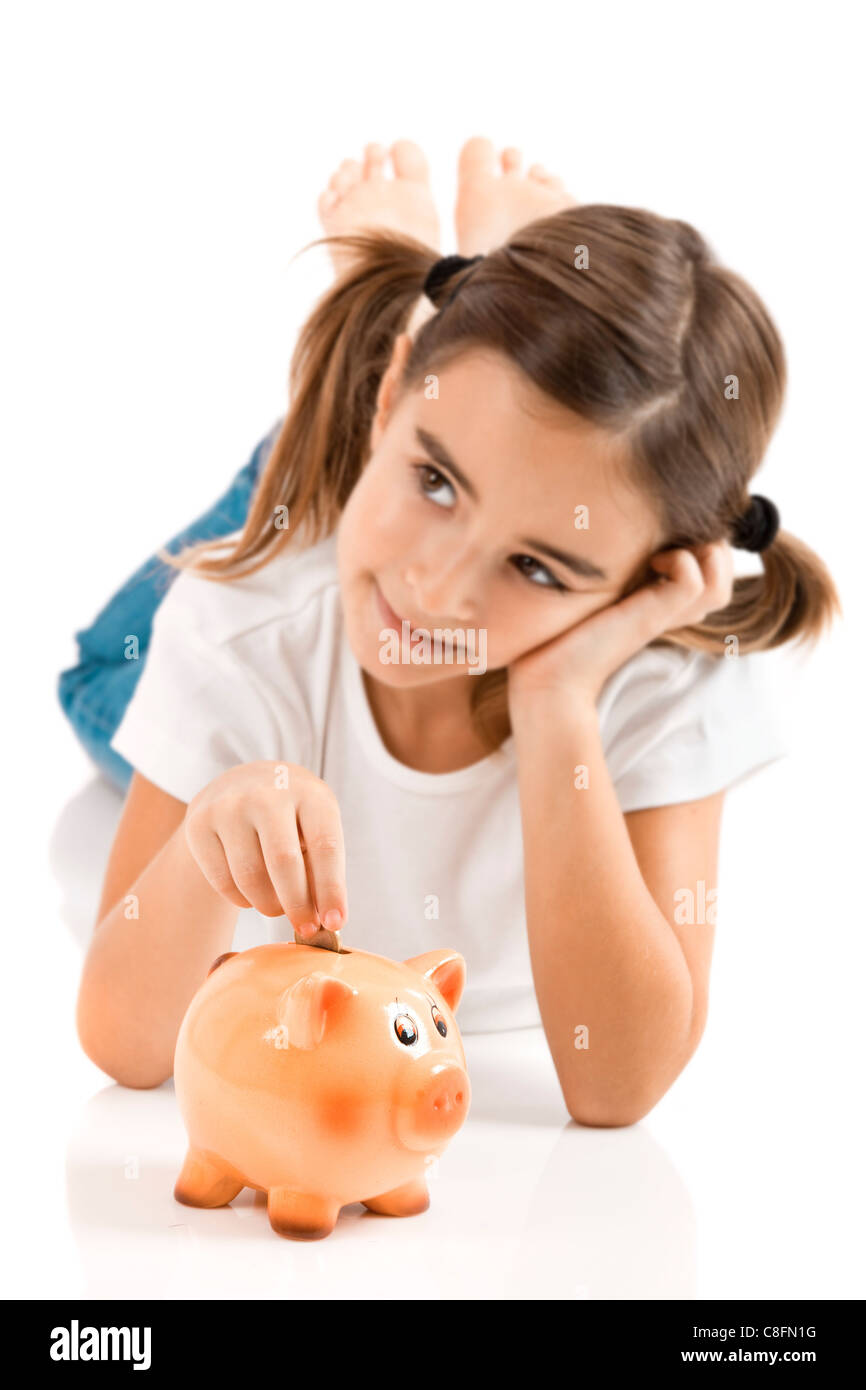 Little girl lying on floor and inserting a one euro coin on the piggy ...