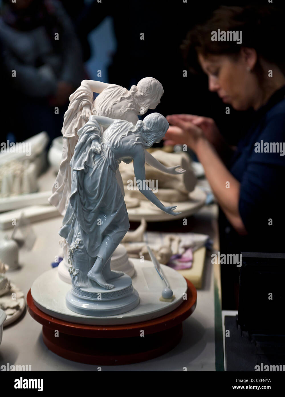 Two Meissen porcelain figure with the craftsperson in the background. Stock Photo
