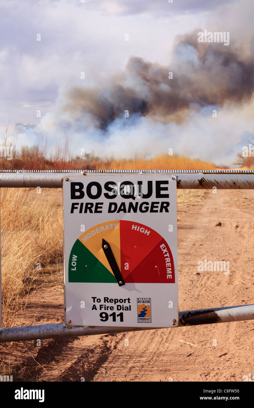 A fire danger sign and wildfire burning in the background in rural New Mexico. Stock Photo