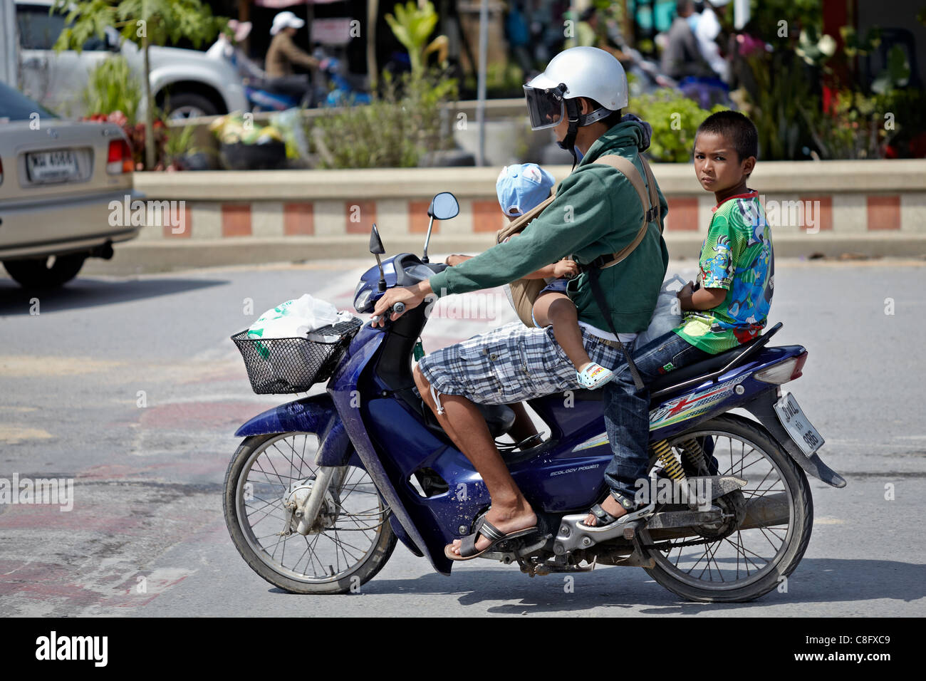 Mother precariously carrying her children on a motorcycle. She is ...