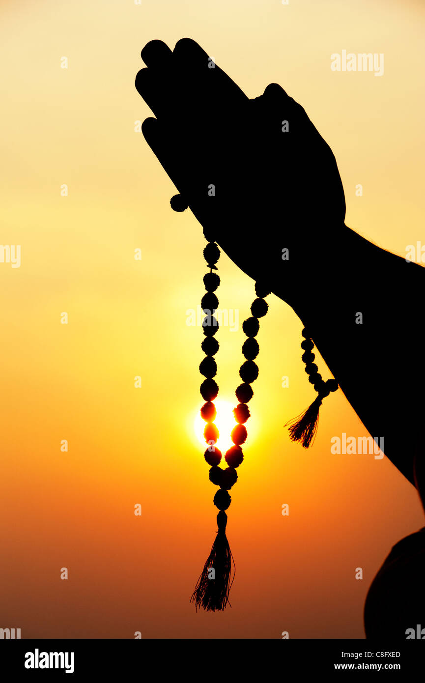 Mans Prayer hands holding Indian Rudraksha / Japa Mala prayer beads . Silhouette Stock Photo